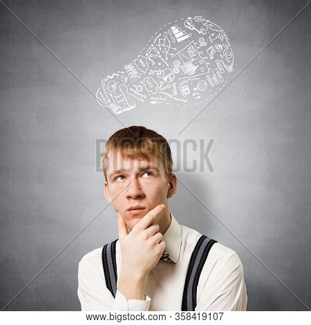Redhead Student Thinking About Some Problem. Clever Boy On Background Of Grey Wall With Idea Lightbu