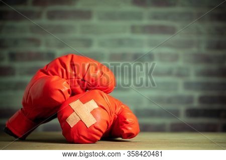Red Boxing Gloves On Wooden Table And Brick Wall At The Sport Gym. Adhesive Plaster Across Each Othe