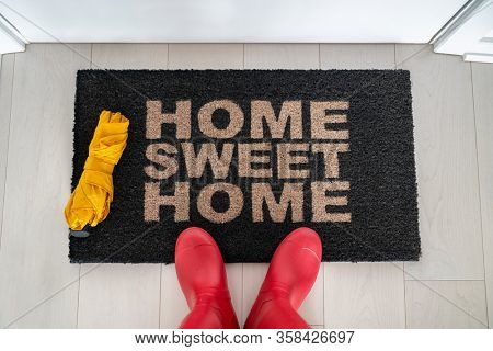 Autumn home sweet home entrance door mat woman taking feet selfie arriving home wiping wet rubber wellington boots and umbrella on rainy day.
