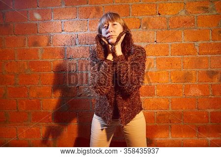 A Middle-aged Woman Poses Showing Clothes Near Red Brick Wall. An Inept Model In An Inept Shoot