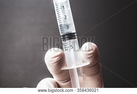Transparent Plastic Syringe Close-up With Transparent Liquid And White Glove. Right Hand Is Holding 