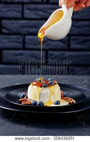 Woman Hand Pouring Dripping Honey On Top Of Baked Soft Brie Cheese With Pecan, Blueberries Served On