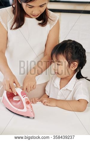 Young Mother Teaching Daughter How To Use Iron