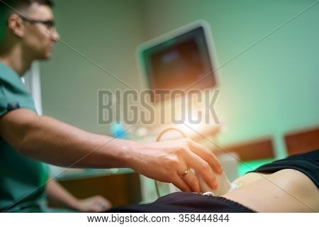 A Young Male Doctor Makes A Patient An Ultrasound Of The Abdominal Cavity. Ultrasound Scanner In The