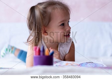 Beautiful Girl Draws With Pencils In Bed. Little Girl Two Years Paints Coloring Book Lying On The Be