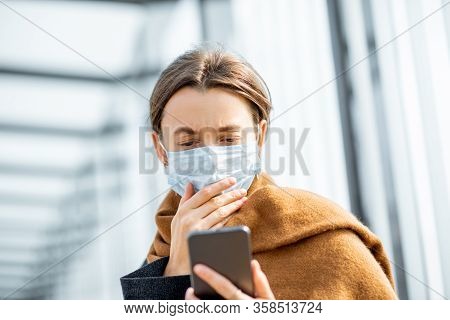 Young And Depressed Woman In Face Mask Worried Reading Bad News On A Smart Phone At A Public Transpo