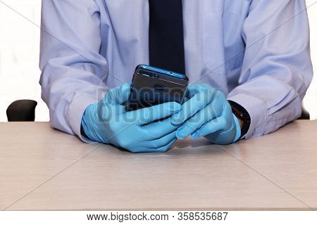 Businessman In Blue Shirt And Tie In Rubber Disposable Gloves With Smartphone.