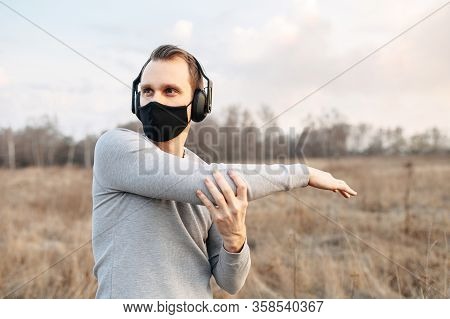 Protect Yourself During A Pandemic. Sports In A Medical Mask. Young Atletic Guy In Headphones Doing 