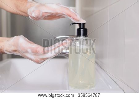 Man Cleaning His Hands Using Liquid Disinfectant Soap And Water In Bathroom.