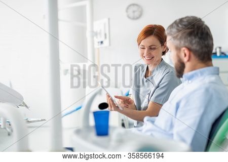 Side View Of Dentist Talking To Man In Dentist Surgery, A Dental Check-up.