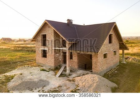 Unfinished Brick House With Wooden Roof Structure Covered With Metal Tile Sheets Under Construction.