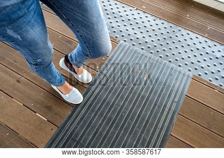 Female Legs In Denim Jeans Pants And Light Summer Sneakers Standing On Wooden Floow.