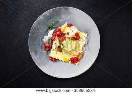 Traditional Italian ravioli pasta offered with parmesan cheese and fried tomatoes as top view on a modern design plate with copy space 