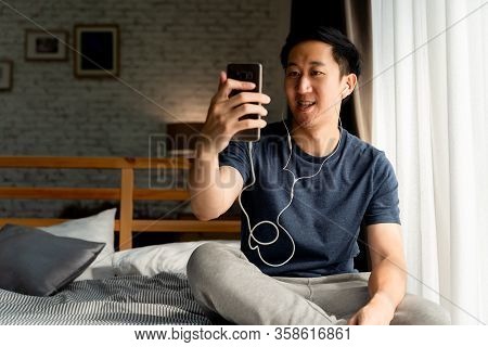 Portrait Of Happy 30s Aged Asian Man In Casual Clothing Making Facetime Video Calling With Smartphon