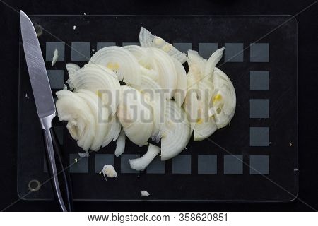 Top View Of Cutted In Half Lengthwise Onion Strips And Kitchen Knife On The Black Background