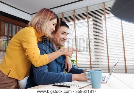 Asian Couple Watching Video Live Straming On Laptop At Table At Home.lover Spending Time Together.ta