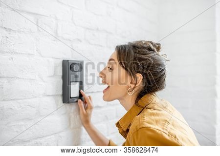 Woman Rings The House Intercom With A Camera Installed On The White Brick Wall