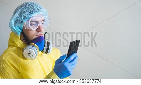 Medical Worker In Protective Gear Using Smartphone After A Shift. Concept Of Covid-19 Epidemic, Heal