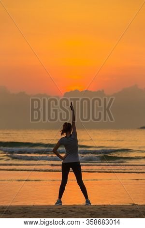 Good Shape Woman Standing And Exercise On Beanch In The Morning With Colorful Sky In Background.