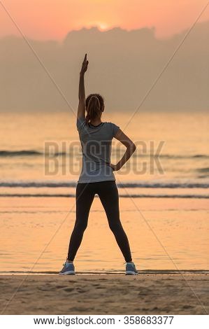 Woman Standing And Exercise On Beanch In The Morning With Colorful Sky And Wave In Background.