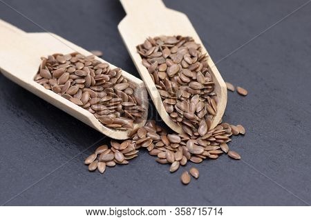 Pile Of Flax Or Flax Seeds In A Wooden Spoon On A Black Stone Background. Dark Background Flaxseed C