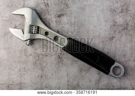 Adjustable Wrench With Black Rubber Handle On Gray Concrete Surface