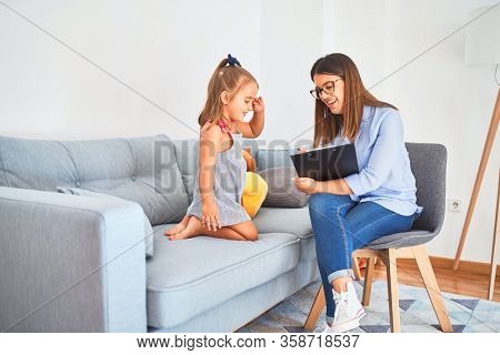 Young therapist woman speaking and treating child, counselor and behaviour correction at pedagogue payroom taking notes on clipboard