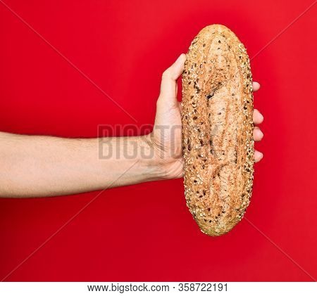 Beautiful hand of man holding wholemeal integral bread with cereals over isolated red background