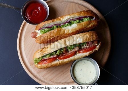 Two Hot Dogs And Sause Lying On The Wooden Plate.