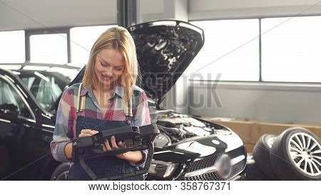 Smiling Young Car Mechanic Is Engaged In Car Diagnostics On A Portative Computer.