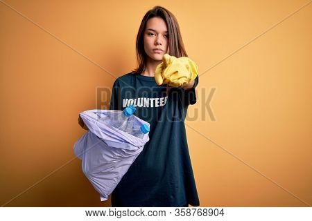 Beautiful volunteer girl caring environment doing volunteering holding bag with rubish bottles pointing with finger to the camera and to you, hand sign, positive and confident gesture from the front