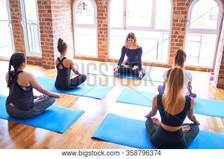 Young beautiful group of sportswomen practicing yoga. Coach teaching lotus pose to sporty women at gym