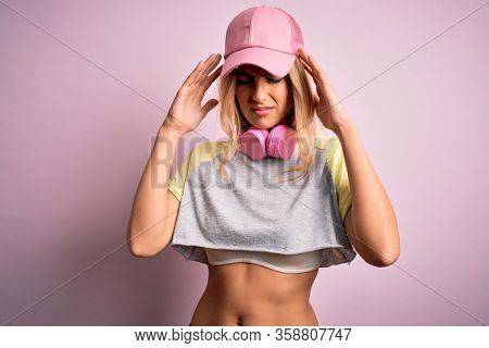 Young beautiful blonde sportswoman doing sport using headphones over pink background suffering from headache desperate and stressed because pain and migraine. Hands on head.