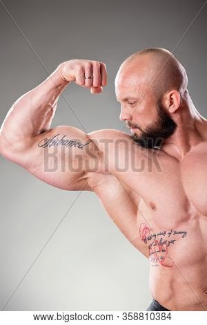 Sexy Muscular Bodybuider Posing On The Gray Background. Biceps Contraction