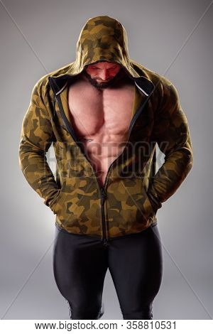 Sexy Muscular Bodybuider Posing With Sweatshirt And Hood On The Gray Background