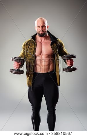 Sexy Muscular Bodybuider Posing With Sweatshirt And Lifting Weights On The Gray Background.