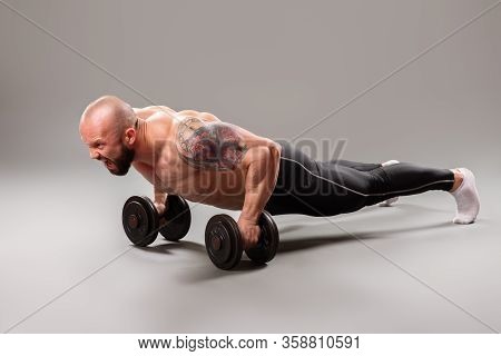 Sexy Muscular Bodybuider Doing Push Ups With Weights On The Gray Background