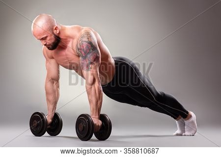 Sexy Muscular Bodybuider Doing Push Ups With Weights On The Gray Background