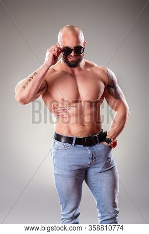 Sexy Muscular Bodybuider With Sunglasses Posing On The Gray Background