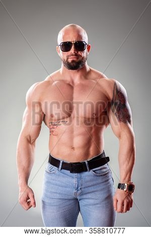 Sexy Muscular Bodybuider With Sunglasses Posing On The Gray Background