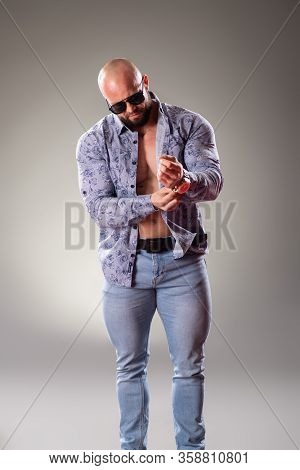 Sexy Muscular Bodybuider With Sunglasses Clothe His Shirt On The Gray Background
