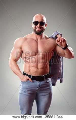 Sexy Muscular Bodybuider With Sunglasses On The Gray Background Throw Off His Shirt