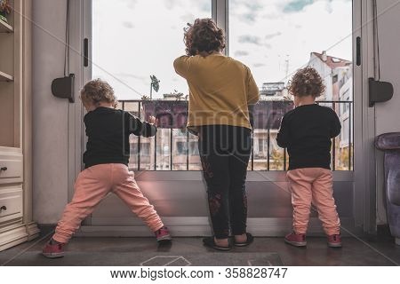 A Boy And His Two Twin Sisters Leaning Against The Window Saddened That They Cannot Go Out To The Pa