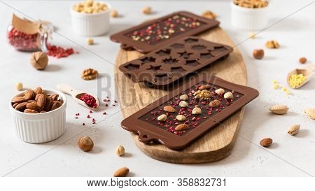 Homemade Dark Chocolate Bars And Pralines In Molds With Dried Berries And Nuts On White Background. 