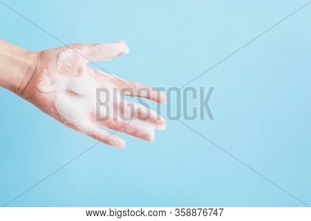Persons Hand In Shower Gel Or Soap Bubbles Isolated On Blue Background. Antibacterial Handwashing. H