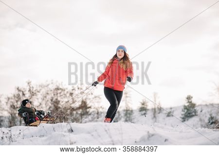 A Father Is Carrying A Child On A Sled. Father Walks With Her Son Over The Snow-covered Forest. Chee