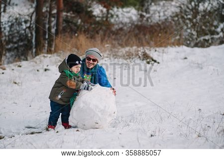 Father And Little Toddler Boy Walking In The Winter Forest And Having Fun With Snow. Family Enjoying
