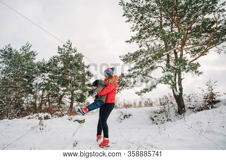 Mother And Little Toddler Boy Walking In The Winter Forest And Having Fun With Snow. Family Enjoying