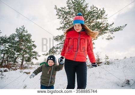 Mother And Little Toddler Boy Walking In The Winter Forest And Having Fun With Snow. Family Enjoying