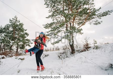 Mother And Little Toddler Boy Walking In The Winter Forest And Having Fun With Snow. Family Enjoying